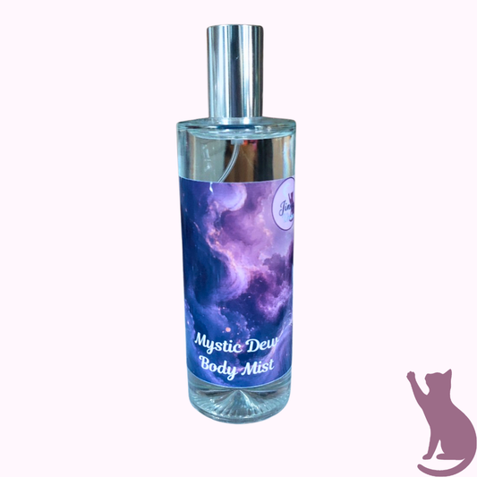 A clear glass bottle of body mist with a silver cap and a purple galaxy-themed label reading 'Mystic Dew Body Mist' on a pale pink background.